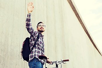people, travel, tourism, gesture and lifestyle - happy young hipster man with fixed gear bike and backpack waving hand on city street