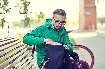 people, style, leisure and lifestyle - young hipster man with backpack sitting on city bench