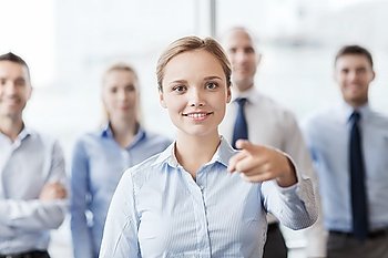business, people and teamwork concept - smiling businesswoman pointing finger on you with group of businesspeople in office