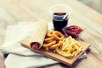 fast food and unhealthy eating concept - close up of deep-fried squid rings, french fries, cola and ketchup on wooden table