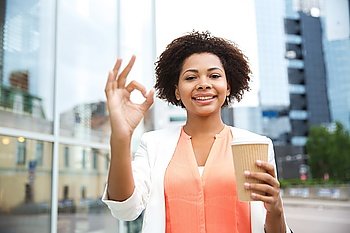 business, drinks, gesture and people concept - young smiling african american businesswoman with coffee cup in city showing  ok sign