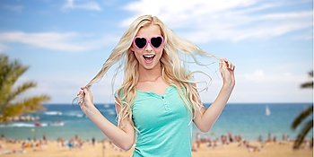 emotions, expressions, summer holidays, travel and people concept - smiling young woman or teenage girl in sunglasses holding her strand of hair over exotic tropical beach and sea background