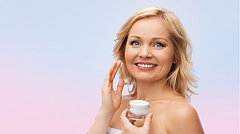 beauty, people, skincare and cosmetics concept - happy woman applying cream to her face over rose quartz and serenity gradient background