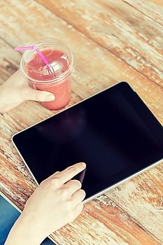 healthy eating, diet, technology and people concept - close up of woman hands with cup of smoothie pointing finger to tablet pc computer black blank screen on wooden table