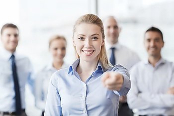 business, people and teamwork concept - smiling businesswoman pointing finger on you with group of businesspeople in office