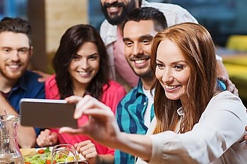 leisure, technology, friendship, people and holidays concept - happy friends having dinner and taking selfie by smartphone at restaurant