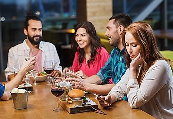 leisure, technology, internet addiction, lifestyle and people concept - woman with smartphone and friends at restaurant