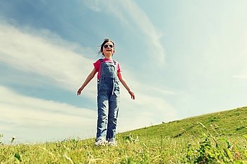 summer, childhood, leisure and people concept - happy little girl over green field and blue sky outdoors