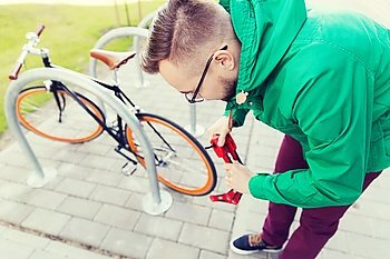 people, security, safety and lifestyle - young hipster man fastening fixed gear bike with blocking lock on city street parking