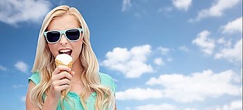 summer, junk food and people concept - young woman or teenage girl in sunglasses eating ice cream over blue sky and clouds background