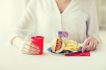 independence day, celebration, patriotism and holidays concept - close up of woman eating hot dog with american flag decoration and potato chips, drinking juice and celebrating 4th july at home party