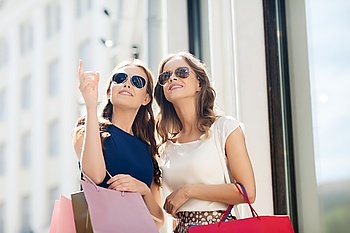 sale, consumerism and people concept - happy young women with shopping bags pointing finger outdoors