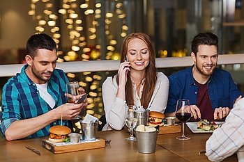 leisure, technology, lifestyle and people concept - happy friends with smartphones calling and texting at dinner in restaurant