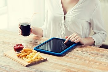 fast food, people, technology and diet concept - close up of woman with tablet pc computer eating french fries with ketchup, deep-fried squid rings and cola at wooden table