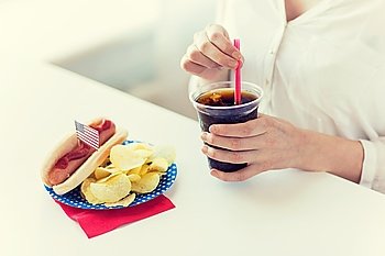 american independence day, celebration, patriotism and holidays concept - close up of woman drinking cola from plastic cup with hot dog and potato chips on 4th july at home party