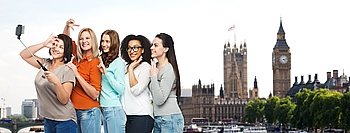 friendship, technology, travel, tourism and people concept - group of happy different size women taking picture with smartphoone on selfie stick over london city and big ben tower background