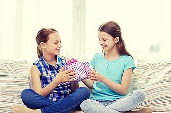 people, children, holidays, friends and friendship concept - happy little girls with birthday present sitting on sofa at home