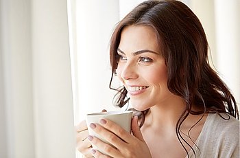 people, drinks and leisure concept - happy young woman with cup of tea or coffee at home