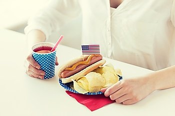 independence day, celebration, patriotism and holidays concept - close up of woman eating hot dog with american flag decoration and potato chips, drinking juice and celebrating 4th july at home party