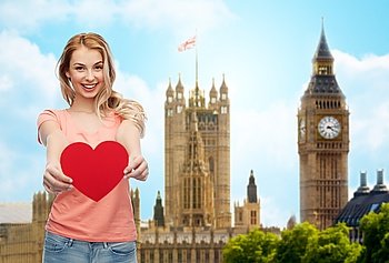 love, travel, tourism, valentines day and people concept - smiling young woman or teenage girl with blank red heart shape over big ben london and city background