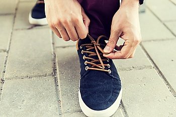 people, footwear and fashion concept - close up of male hands tying shoe laces on street