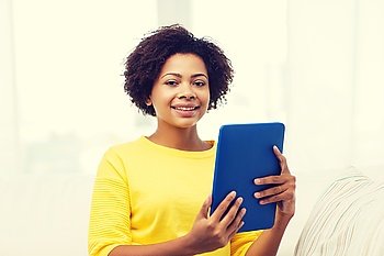 people, technology and leisure concept - happy african american young woman sitting on sofa with tablet pc computer at home