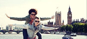 friendship, leisure, international, freedom and people concept - happy teenage couple in shades having fun over houses of parliament and thames river in london background