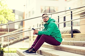 people, style, technology and lifestyle - young hipster man with smartphone sitting on stairs in city