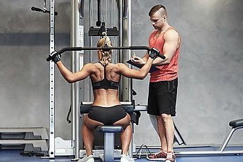sport, fitness, teamwork and people concept - young woman and personal trainer flexing muscles on gym machine
