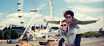 friendship, leisure, international, freedom and people concept - happy teenage couple in shades having fun over london ferry wheel background