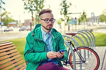 people, style, technology and lifestyle - happy young hipster man with smartphone and fixie bike sitting on bench in city