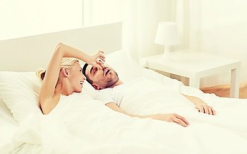 people, family, bedtime and couple concept - happy woman closing nose to her snoring man sleeping in bed at home