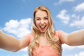 emotions, expressions and people concept - happy smiling young woman taking selfie over blue sky and clouds background
