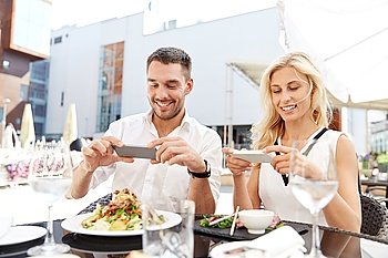 love, date, technology, people and relations concept - happy couple with smatphone taking picture of food at restaurant terrace