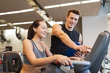 sport, fitness, lifestyle, technology and people concept - happy woman with trainer working out on exercise bike in gym