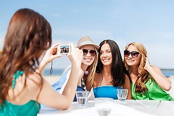summer holidays and vacation - girls taking photo with digital camera in cafe on the beach. girls taking photo in cafe on the beach