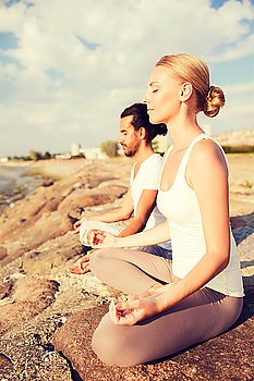 fitness, sport, friendship and lifestyle concept - smiling couple making yoga exercises sitting outdoors