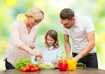 vegetarian food, culinary, happiness and people concept - happy family cooking vegetable salad for dinner over green lights background