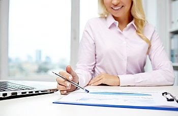 education, business, people and technology concept - close up of smiling businesswoman with laptop computer and papers sitting in office