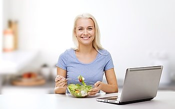 healthy eating, dieting and people concept - smiling young woman with laptop computer eating vegetable salad over kitchen background
