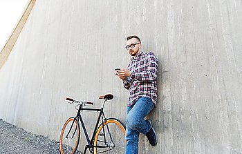 people, style, technology, leisure and lifestyle - happy young hipster man in earphones with smartphone and fixed gear bike listening to music on city street