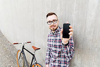 people, technology, leisure, advertisement and lifestyle - happy young hipster man in earphones with fixed gear bike listening to music and showing smartphone black blank screen on city street