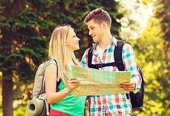 travel, vacation, tourism and friendship concept - smiling couple with map and backpacks looking at each other in forest