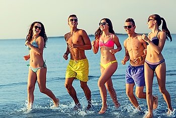 friendship, sea, summer vacation, holidays and people concept - group of smiling friends wearing swimwear and sunglasses running on beach