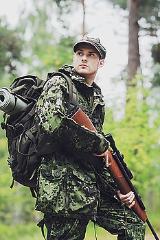 hunting, war, army and people concept - young soldier, ranger or hunter with gun in forest