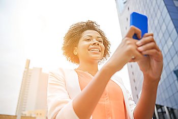 business, technology, communication and people concept - young smiling african american businesswoman with smartphone in city