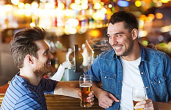 people, men, leisure, friendship and communication concept - happy male friends drinking beer and talking at bar or pub