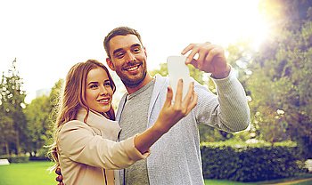 love, relationship, technology and people concept - happy couple with smartphone taking selfie in summer park
