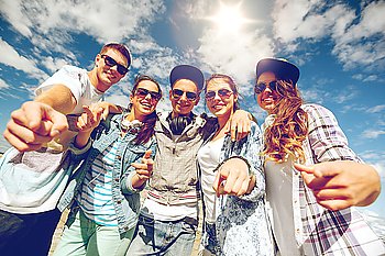 summer holidays and teenage concept - group of smiling teenagers in sunglasses hanging outside pointing finger at you. smiling teenagers in sunglasses hanging outside