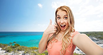 travel, tourism, emotions, expressions and people concept - happy smiling young woman taking selfie and showing thumbs up over exotic tropical beach background